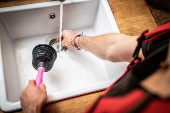 سباك يستخدم أنبوب المكبس لإصلاح حوض المطبخ