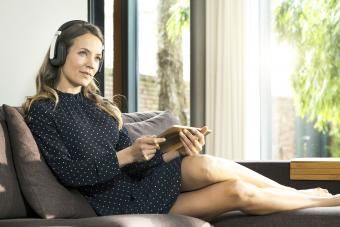 Mulher com tablet e fones de ouvido relaxando no sofá em casa