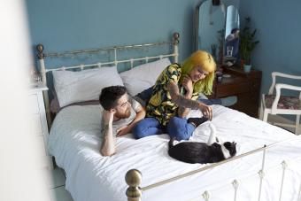 Unge hipsterpar liggende på deres seng sammen og leger med deres kattekat