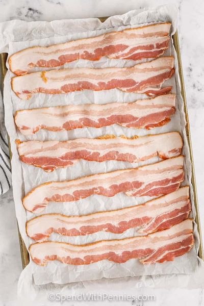 bacon em uma assadeira com pergaminho para mostrar como cozinhar bacon no forno