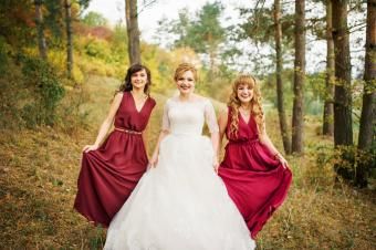 Noiva com damas de honra em vestidos vermelhos em um bosque de pinheiros de outono